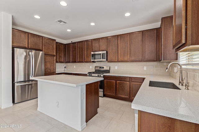 kitchen featuring appliances with stainless steel finishes, sink, light stone countertops, backsplash, and a center island