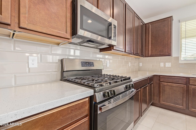 kitchen with light tile patterned flooring, light stone counters, stainless steel appliances, and backsplash