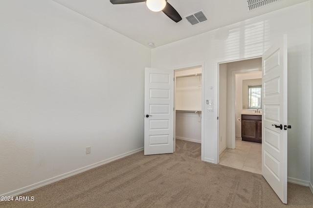 unfurnished bedroom with a spacious closet, light carpet, a closet, and ceiling fan