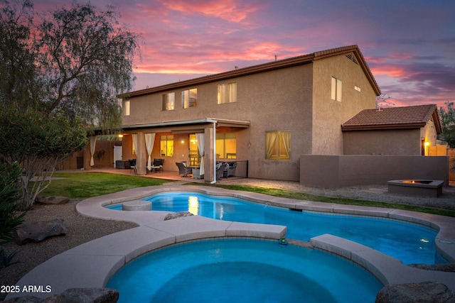 pool at dusk featuring a patio area, a pool with connected hot tub, and an outdoor fire pit