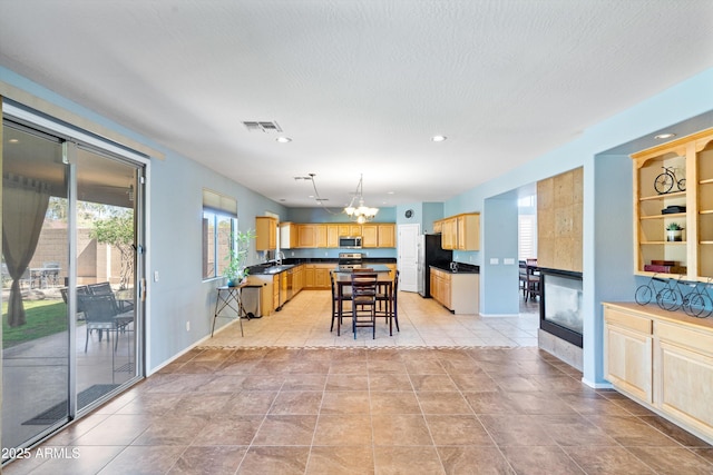 kitchen with an inviting chandelier, light brown cabinetry, appliances with stainless steel finishes, a kitchen bar, and dark countertops