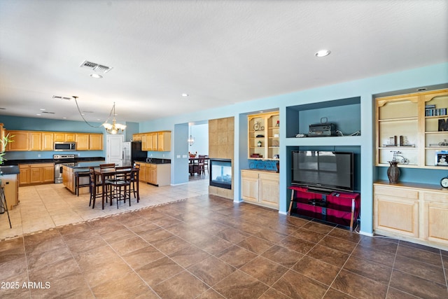 kitchen with dark countertops, visible vents, light brown cabinetry, an inviting chandelier, and stainless steel appliances