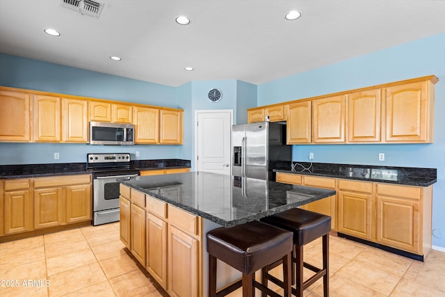 kitchen featuring visible vents, light brown cabinets, a breakfast bar area, dark stone counters, and appliances with stainless steel finishes