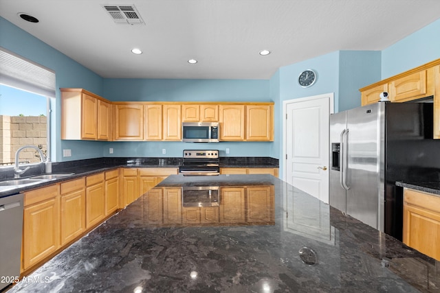 kitchen featuring visible vents, light brown cabinets, dark stone counters, stainless steel appliances, and a sink