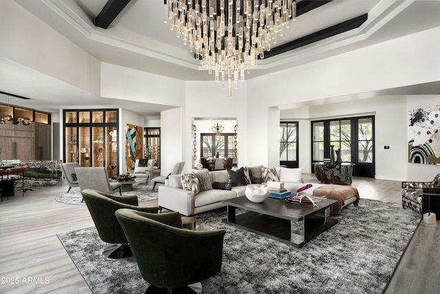 living room with an inviting chandelier, a high ceiling, a tray ceiling, and wood finished floors