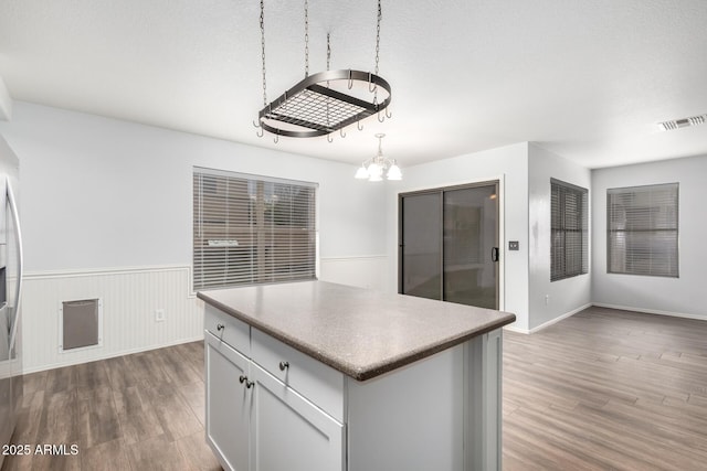 kitchen featuring a wainscoted wall, visible vents, wood finished floors, and a center island