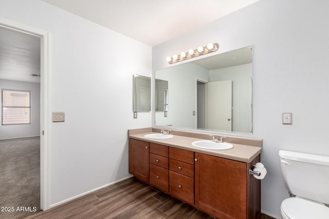 full bathroom with toilet, double vanity, a sink, and wood finished floors