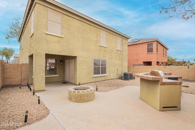 back of property with central air condition unit, stucco siding, a patio area, exterior kitchen, and a fenced backyard