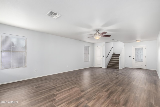 unfurnished living room featuring dark wood-style floors, visible vents, baseboards, and stairs