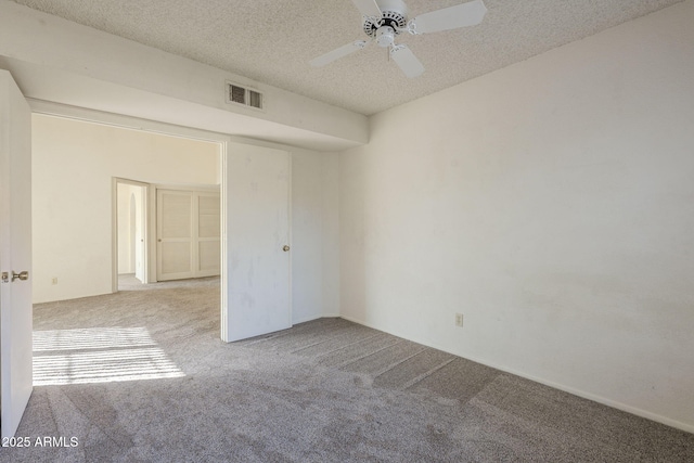 spare room featuring a ceiling fan, visible vents, a textured ceiling, and light colored carpet