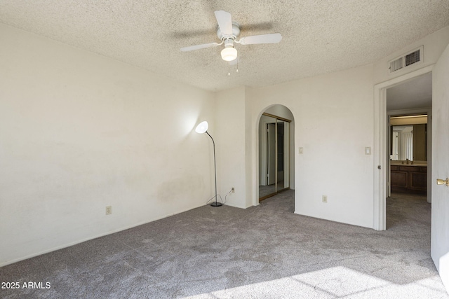 empty room featuring arched walkways, ceiling fan, a textured ceiling, light carpet, and visible vents