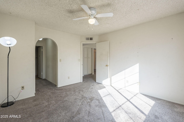 spare room with arched walkways, visible vents, a ceiling fan, light carpet, and a textured ceiling