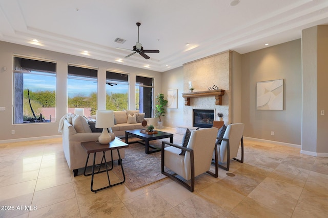 living room featuring a raised ceiling, ceiling fan, and a large fireplace