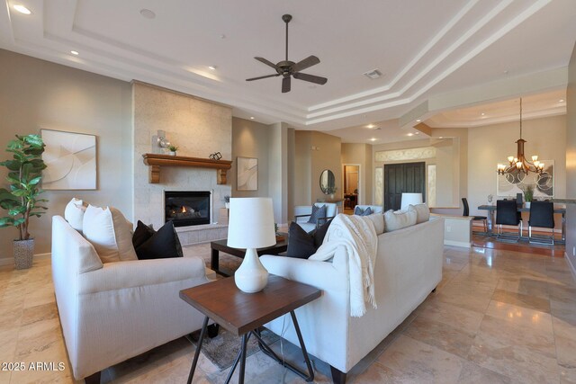 living room with a raised ceiling, a fireplace, and ceiling fan with notable chandelier