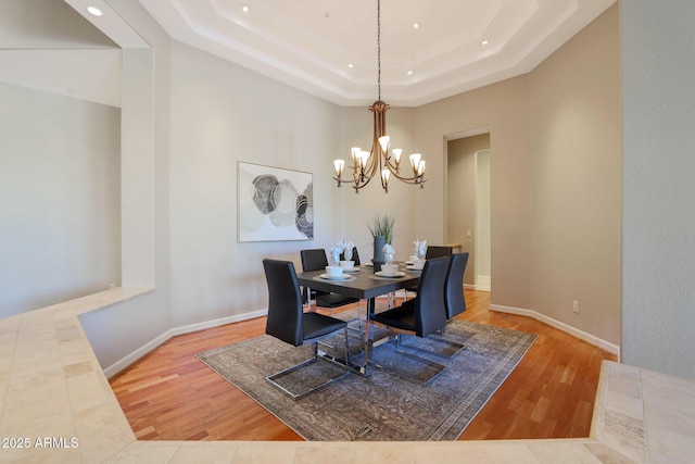 dining area featuring wood-type flooring, a tray ceiling, and an inviting chandelier