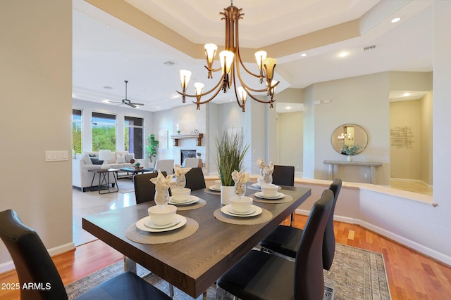 dining room featuring light wood-type flooring, ceiling fan with notable chandelier, and a tray ceiling