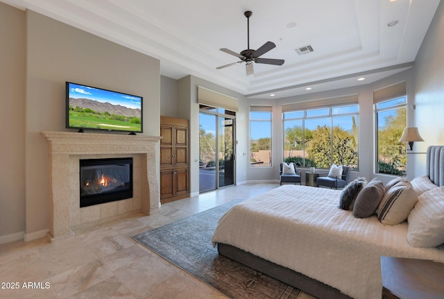 bedroom featuring access to outside, multiple windows, ceiling fan, and a tray ceiling