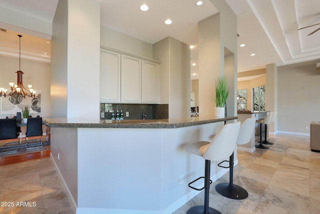 kitchen with kitchen peninsula, a kitchen breakfast bar, backsplash, ceiling fan with notable chandelier, and white cabinets