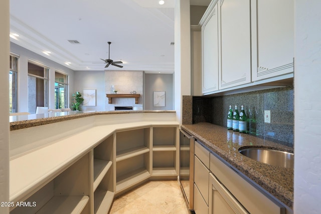 kitchen featuring backsplash, dark stone counters, sink, ceiling fan, and white cabinetry