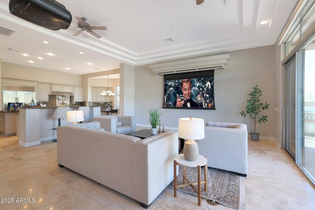 living room featuring ceiling fan with notable chandelier, a wealth of natural light, and a tray ceiling