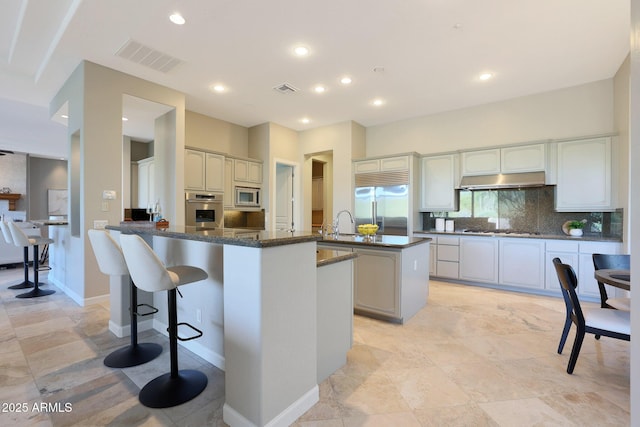 kitchen featuring sink, backsplash, kitchen peninsula, built in appliances, and a kitchen bar