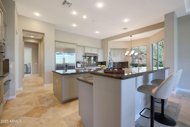 kitchen with a center island with sink, a kitchen breakfast bar, decorative light fixtures, a notable chandelier, and stainless steel built in refrigerator