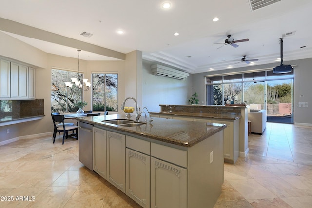 kitchen featuring dishwasher, sink, dark stone countertops, decorative light fixtures, and a center island with sink