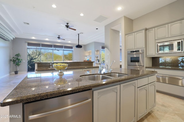 kitchen with sink, stainless steel appliances, decorative backsplash, dark stone countertops, and a kitchen island with sink