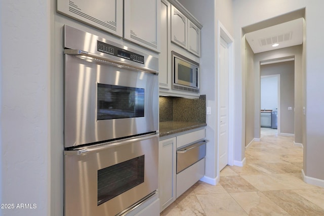 kitchen featuring appliances with stainless steel finishes, tasteful backsplash, gray cabinetry, and dark stone countertops