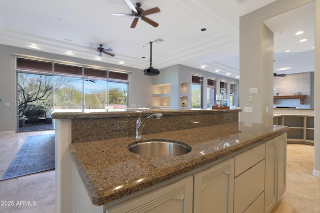 kitchen featuring ceiling fan, a center island, sink, and stone counters