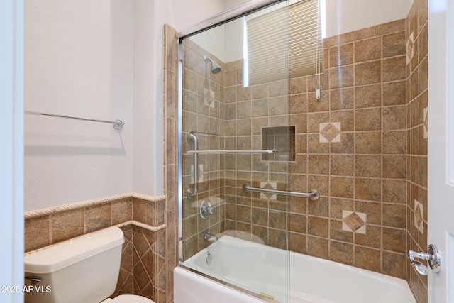 bathroom featuring toilet, bath / shower combo with glass door, and tile walls