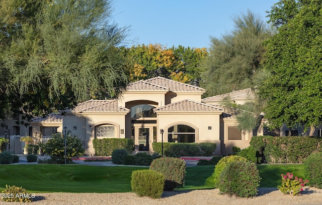 mediterranean / spanish house featuring a tiled roof, a front lawn, and stucco siding