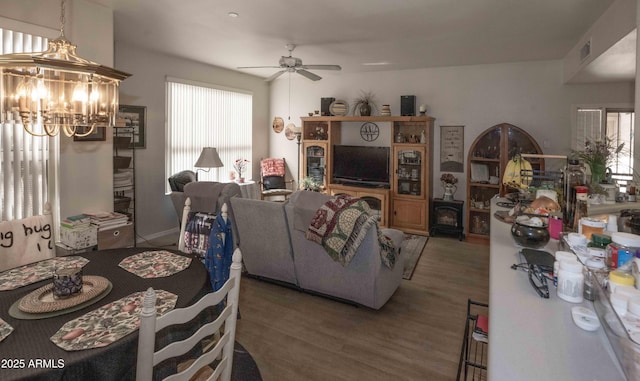 living area with ceiling fan with notable chandelier, a wood stove, wood finished floors, and visible vents