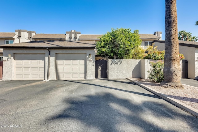 view of front of home with stucco siding, aphalt driveway, an attached garage, and fence