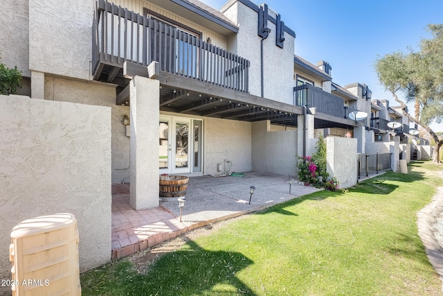 exterior space featuring a wooden deck, stucco siding, french doors, a lawn, and a patio