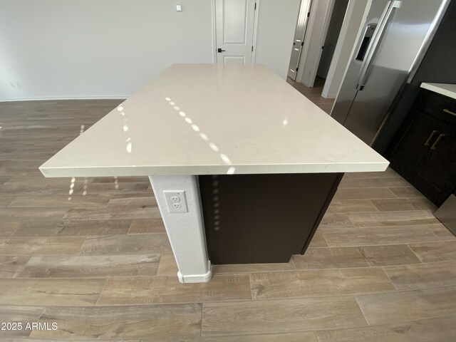 kitchen featuring wood finished floors, a kitchen island, baseboards, light countertops, and stainless steel fridge with ice dispenser