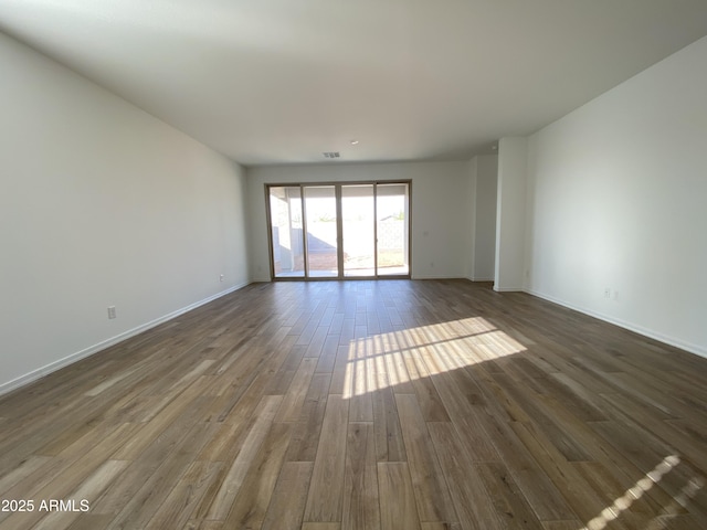 empty room featuring dark wood-type flooring, visible vents, and baseboards