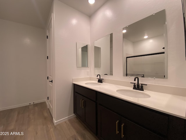 bathroom featuring double vanity, a shower stall, a sink, and wood finished floors