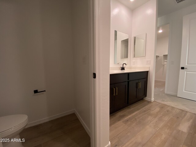 bathroom featuring visible vents, toilet, vanity, wood finished floors, and baseboards