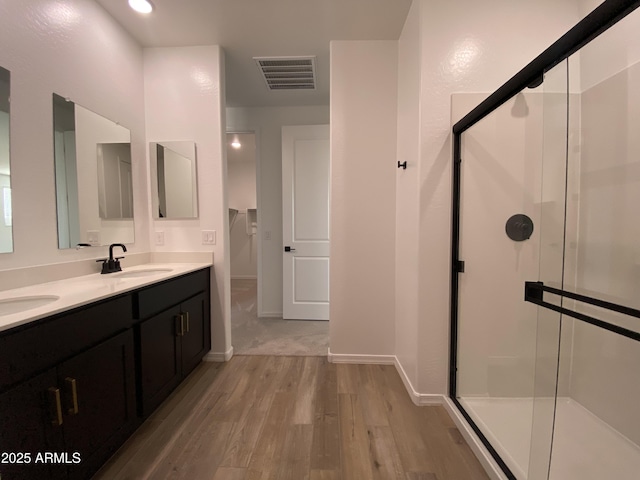 full bathroom with double vanity, visible vents, a sink, a shower stall, and wood finished floors