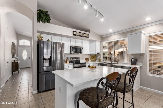 kitchen with a kitchen breakfast bar, vaulted ceiling, a kitchen island, white cabinetry, and stainless steel appliances