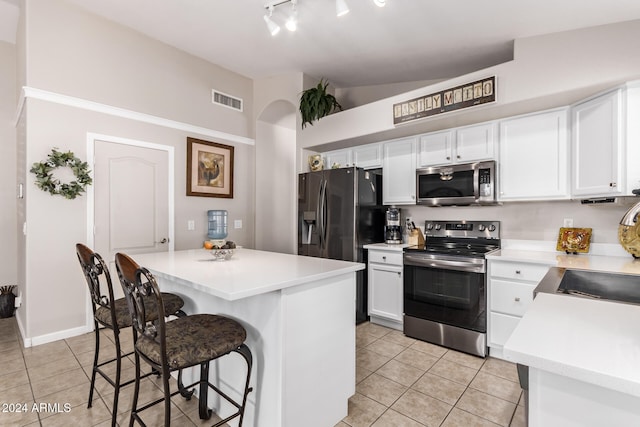 kitchen featuring vaulted ceiling, appliances with stainless steel finishes, light tile patterned flooring, a kitchen bar, and white cabinetry