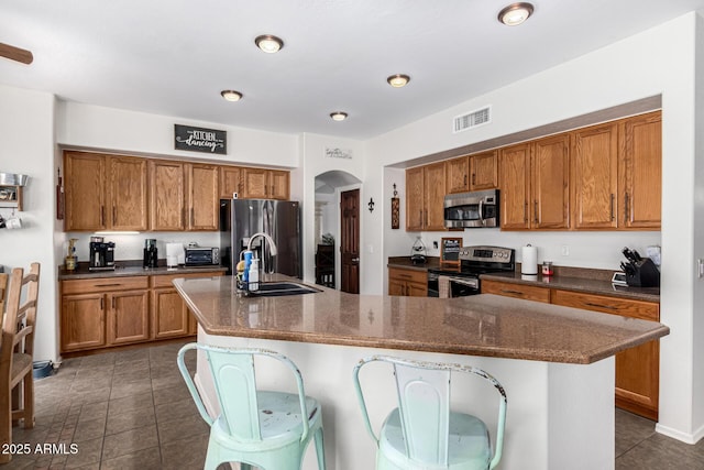 kitchen with visible vents, arched walkways, appliances with stainless steel finishes, brown cabinets, and a sink