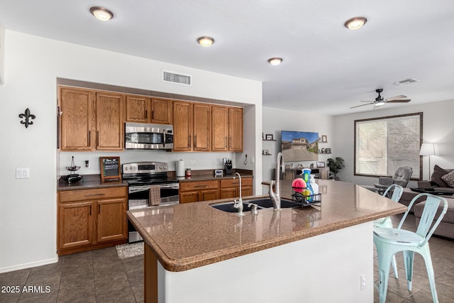 kitchen featuring visible vents, brown cabinetry, a kitchen island with sink, stainless steel appliances, and a sink