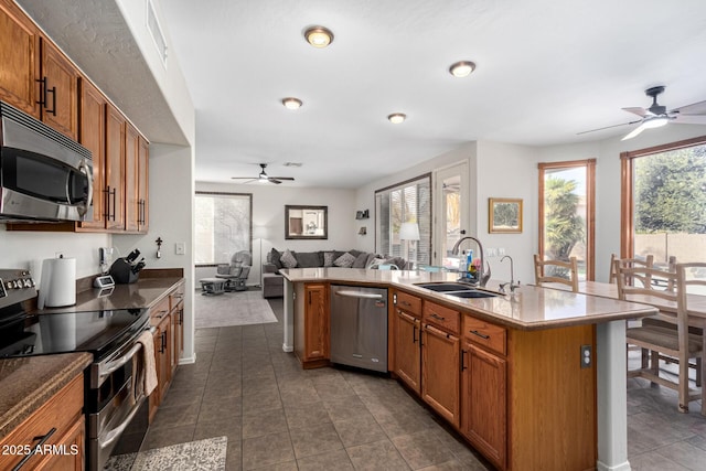 kitchen featuring dark tile patterned floors, a sink, open floor plan, appliances with stainless steel finishes, and brown cabinetry