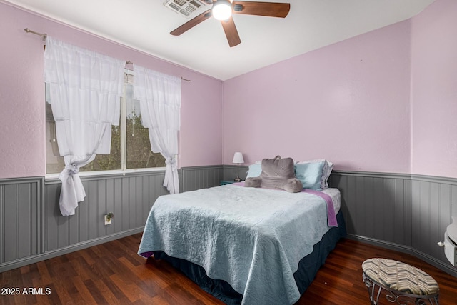 bedroom featuring a ceiling fan, a wainscoted wall, visible vents, and wood finished floors