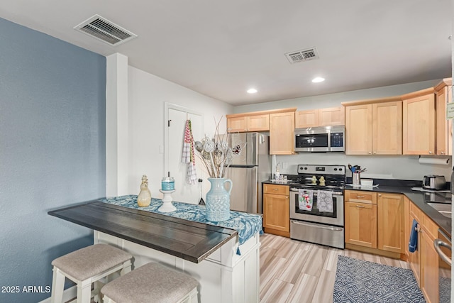 kitchen featuring appliances with stainless steel finishes, a kitchen bar, and light hardwood / wood-style flooring