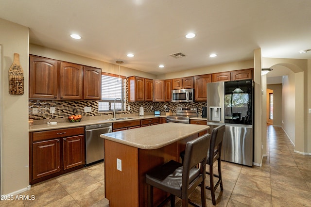 kitchen featuring decorative backsplash, appliances with stainless steel finishes, sink, a kitchen island, and a breakfast bar area