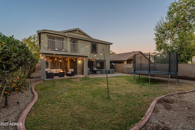 back house at dusk featuring an outdoor hangout area, a balcony, a patio, a yard, and a trampoline