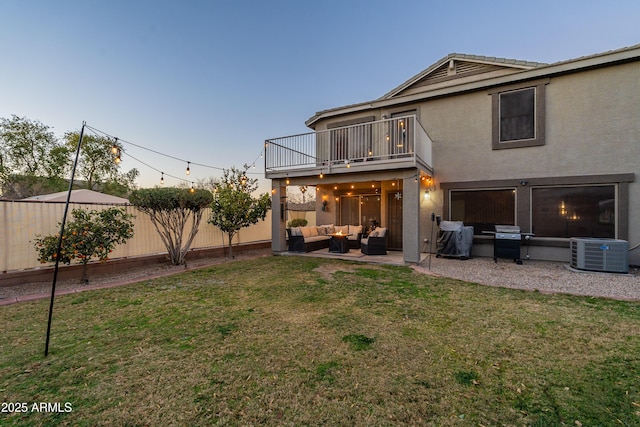 back house at dusk with a yard, outdoor lounge area, a balcony, and central AC unit